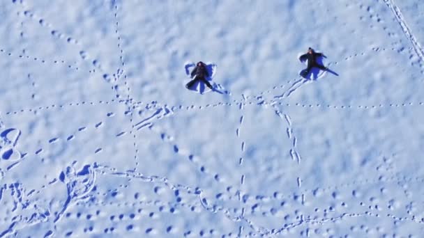 Два хлопці лежать на снігу і грають снігового ангела — стокове відео