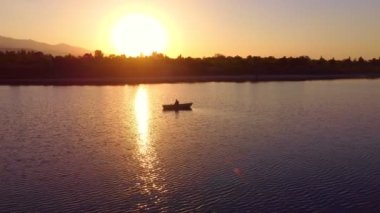 Balıkçılık yaparken teknesinde güzel bir günbatımının keyfini çıkaran tek bir balıkçının silueti. Kırgızistan Gölü Issyk-Kul
