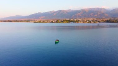 Balıkçılık yaparken teknesinde güzel bir günbatımının keyfini çıkaran tek bir balıkçının silueti. Kırgızistan Gölü Issyk-Kul