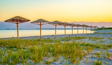 Sahilde güneşin dört köşeli şemsiyesi doğal malzemeler, bambu ve kamışlardan yapılmıştır. Deniz ve kumlu sahil zeminine karşı..