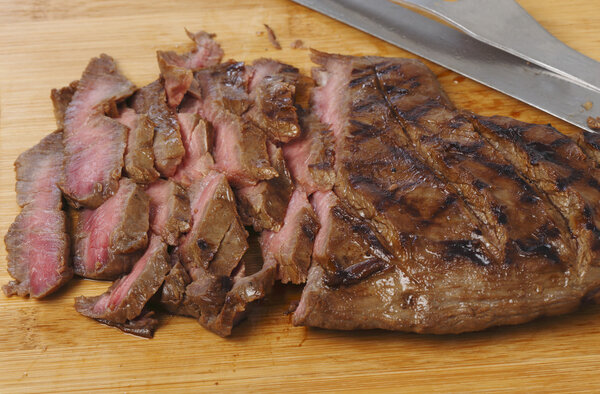 Marinaded flank steak, or London broil, sliced thinly against the grain on a wooden chopping board.