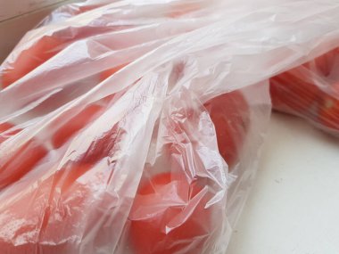 Kırmızı domatesleri beyaz masadaki selofan bir çantaya koy..