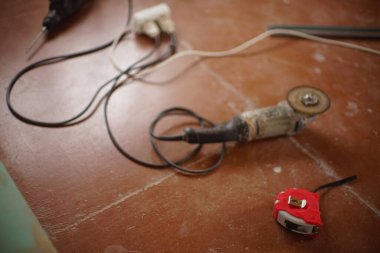 Kırmızı metre, aşındırıcı kesme diski ve kahverengi ahşap zemindeki diğer aletlerle öğütme aracı.