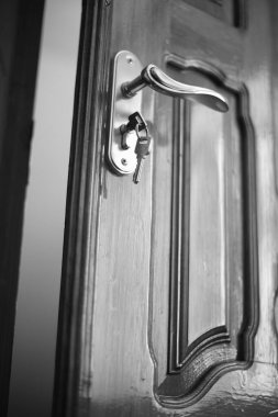 Close-up of lacquered wooden door with handle and key. BW photo.