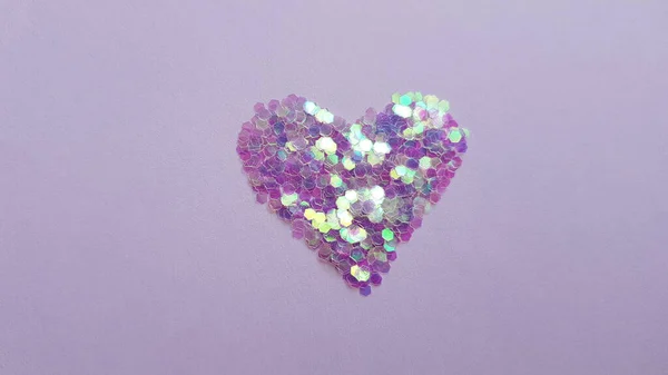 Purple heart made of sequins on a pale lilac table.