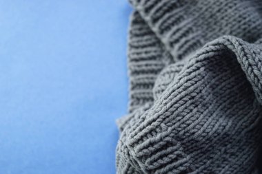 Cozy gray knitted sweater on blue table, copy space, flatlay