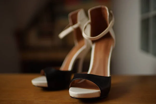 Black and white heeled sandals stand on the wooden floor.