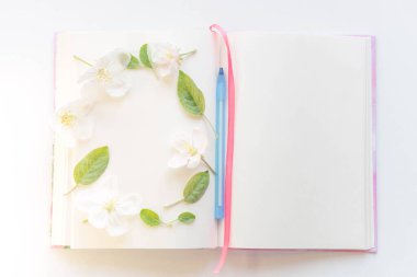 Beyaz çarşaflı açık bir kitap ve elma çiçeklerinde mavi bir kalem..