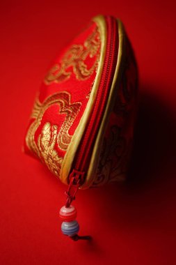 Red cosmetic bag with golden embroidery on the red table.