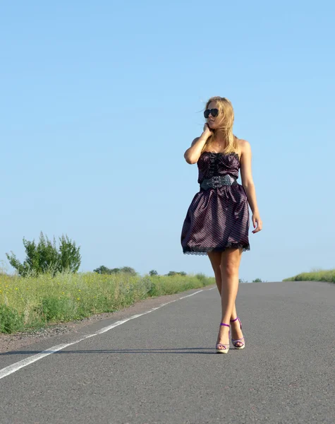 Mulher na moda que anda em uma estrada de país — Fotografia de Stock