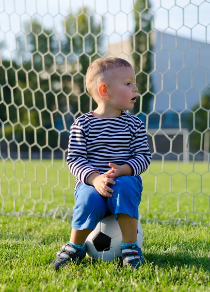 bir futbol topu üzerinde oturan küçük çocuk