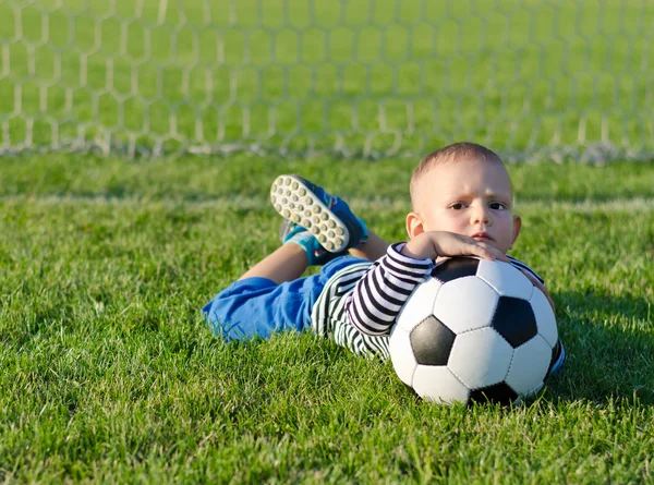 Menino deitado na grama com bola de futebol — Fotografia de Stock