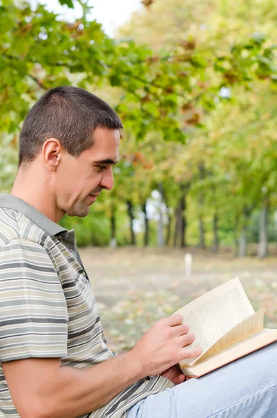 Man sitting outdoors reading a novel — Stock Photo, Image