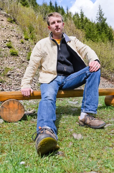 Blonďatý mladík seděl na dřevěné lavičce — Stock fotografie