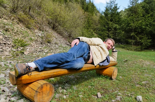 Mladý blonďák muž položil na bok na lavičce — Stock fotografie