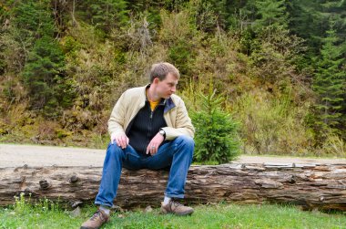 Young man sitting on a tree trunk in nature clipart