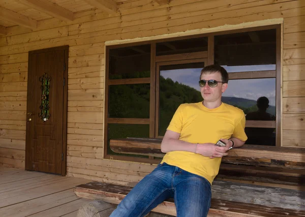 Man sitting in front of a wooden cabin — Stock Photo, Image