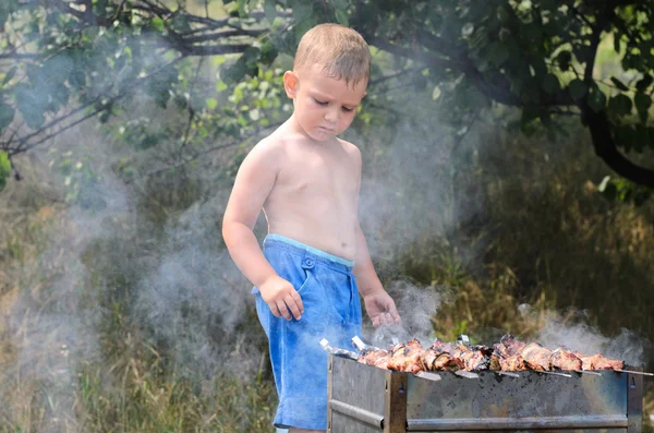 Ładny chłopczyk gotowania mięsa na ogniu — Zdjęcie stockowe