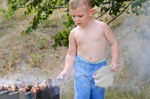 Malý chlapec obrací kebab na ohni — Stock fotografie