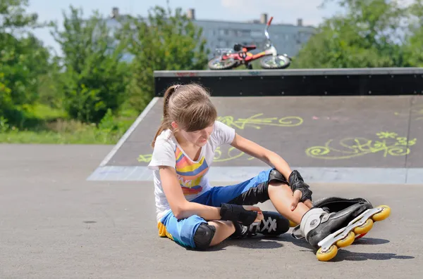 Young girl wearing rollerblades massaging her calf — Stock Photo, Image