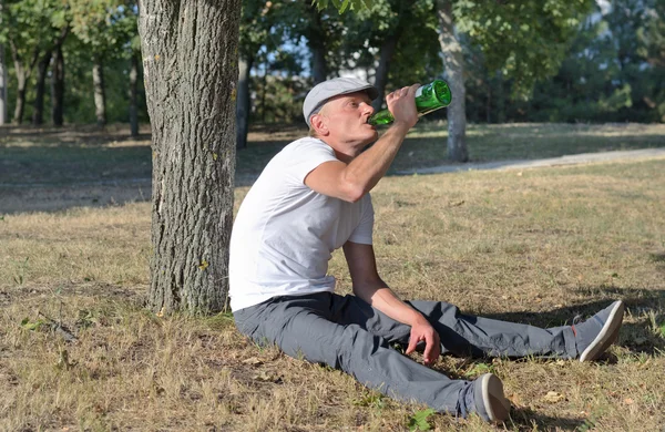 Alcohólico sentado bebiendo en un parque — Foto de Stock