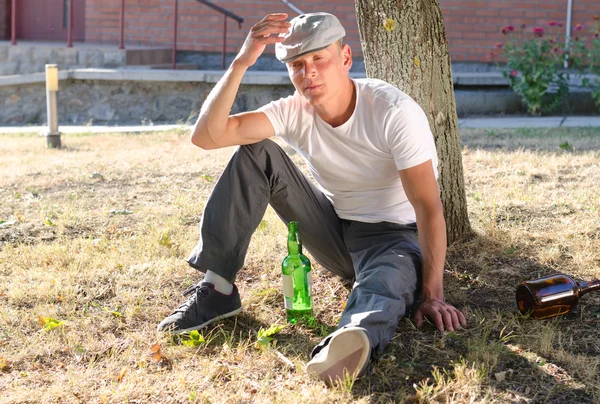 Drunk man sitting at the base of a tree — Stock Photo, Image