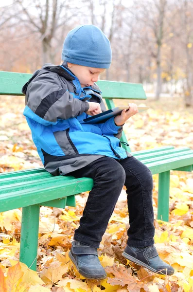 Lille dreng læser en tablet computer i parken - Stock-foto