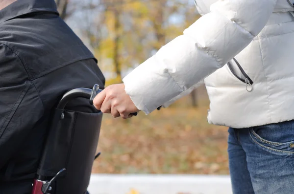 Woman pushing a disabled man in a wheelchair — Stock Photo, Image