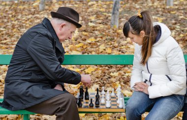 Elderly man arguing during a game of chess with woman sit together on a wooden park bench clipart