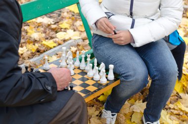 Elderly man a game of chess with woman sit together on a wooden park bench clipart