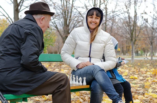 Atractiva mujer sonriente sentada en un banco del parque jugando ajedrez con un anciano — Foto de Stock