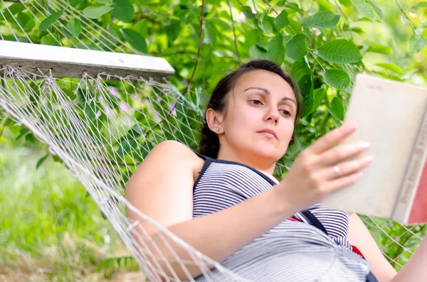 Mujer leyendo mientras se relaja en una hamaca —  Fotos de Stock