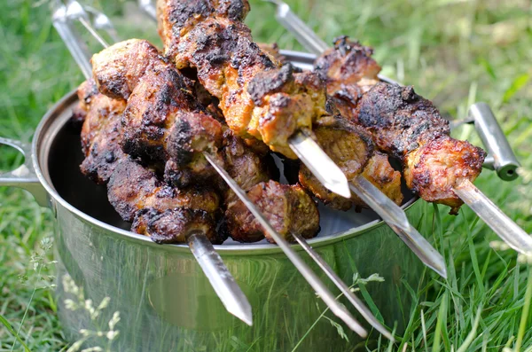 Barbecued food on metal skewers resting on a pot — Stock Photo, Image