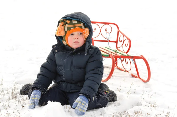 Petit garçon agenouillé dans la neige avec un traîneau — Photo