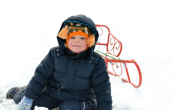 Menino pequeno ajoelhado na neve com um trenó — Fotografia de Stock