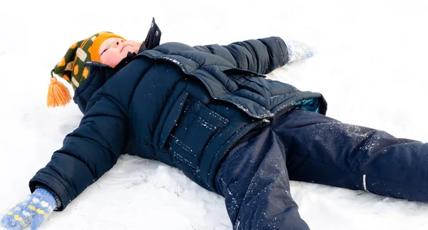 Happy little boy making snow angels in the snow