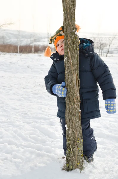 Kleiner Junge schmollt und versteckt sich hinter einem Baumstamm — Stockfoto