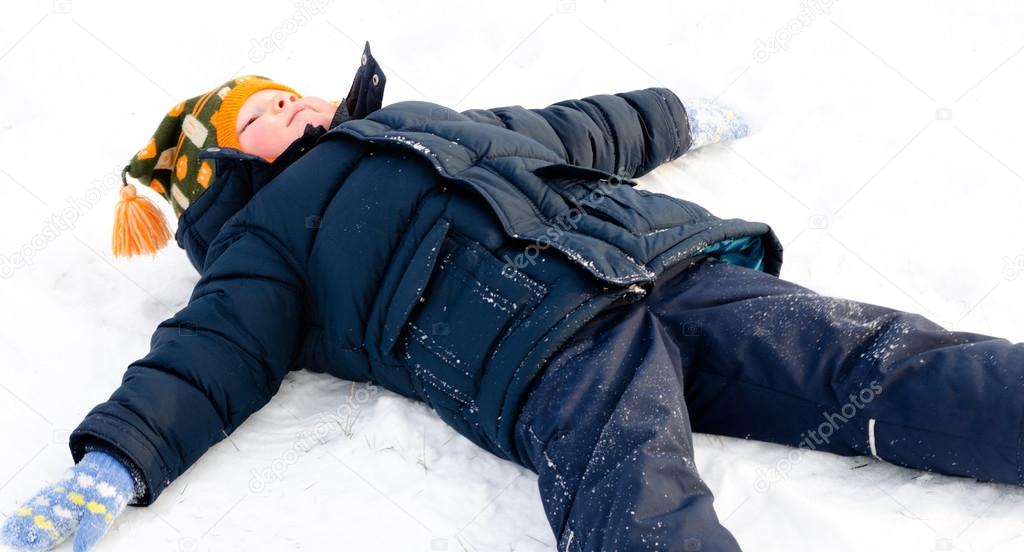 Happy little boy making snow angels in the snow