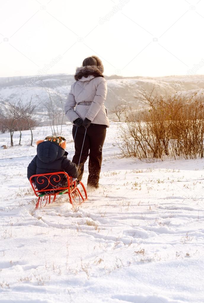 Mother pulling a toboggan with her child in snow