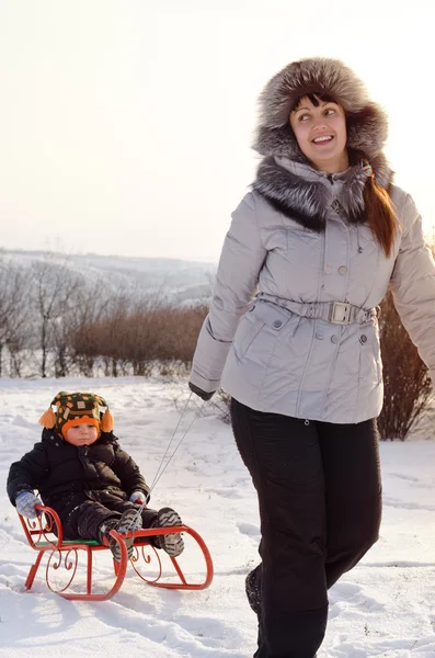 Madre tirando uno slittino con il suo bambino nella neve — Foto Stock