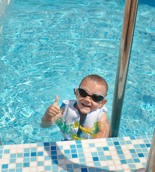 Glad goung pojke i en pool som ger tummen upp — Stockfoto