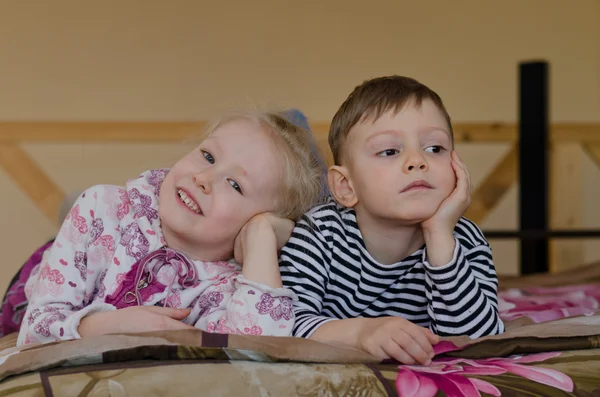 Young brother and sister lying on a bed together — Stock Photo, Image