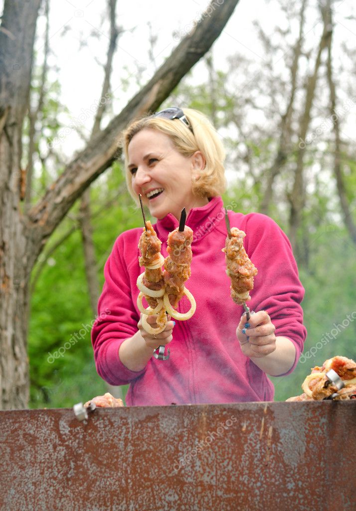 Smiling woman cooking kebabs over a BBQ fire