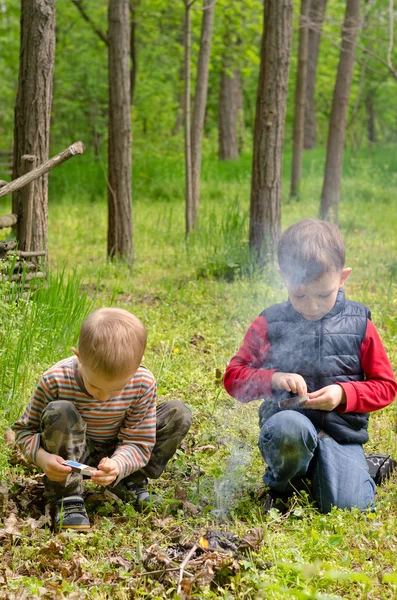 Dos niños pequeños encendiendo un fuego en el bosque — Foto de Stock