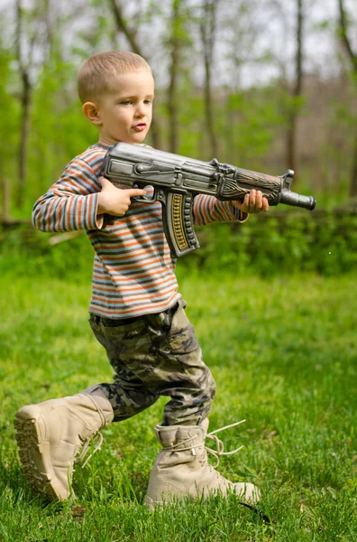 Boy carrying a machine gun saluting — Stock Photo, Image