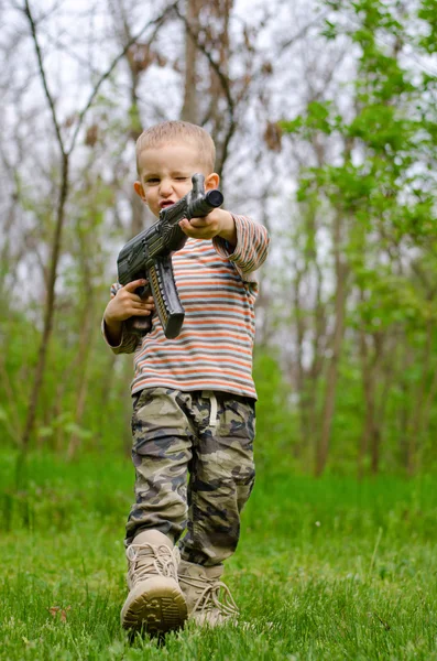 Boy carrying a machine gun saluting — Stock Photo, Image