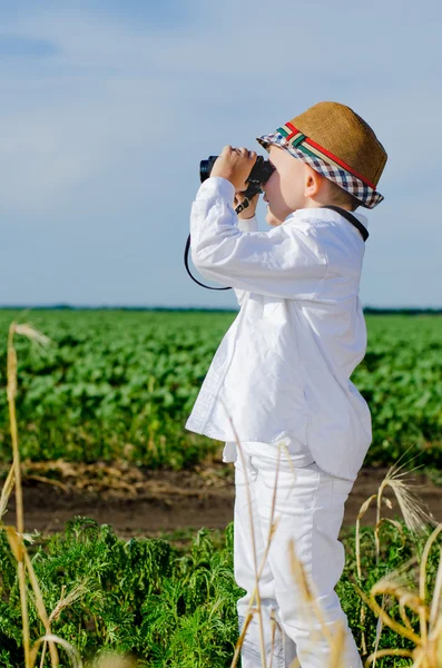 Liten pojke står i jordbruksmark med kikare — Stockfoto