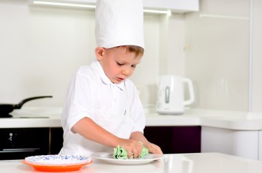küçük çocuk aşçı yemek yaparken onun plakasını temizlik