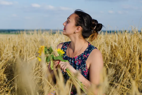Skrattar kvinna med blommor i ett vete fält — Stockfoto
