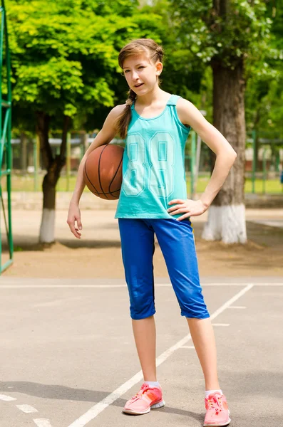 Krásná usměvavá dívka stojící s basketbal v venkovní basketbalové hřiště — Stock fotografie